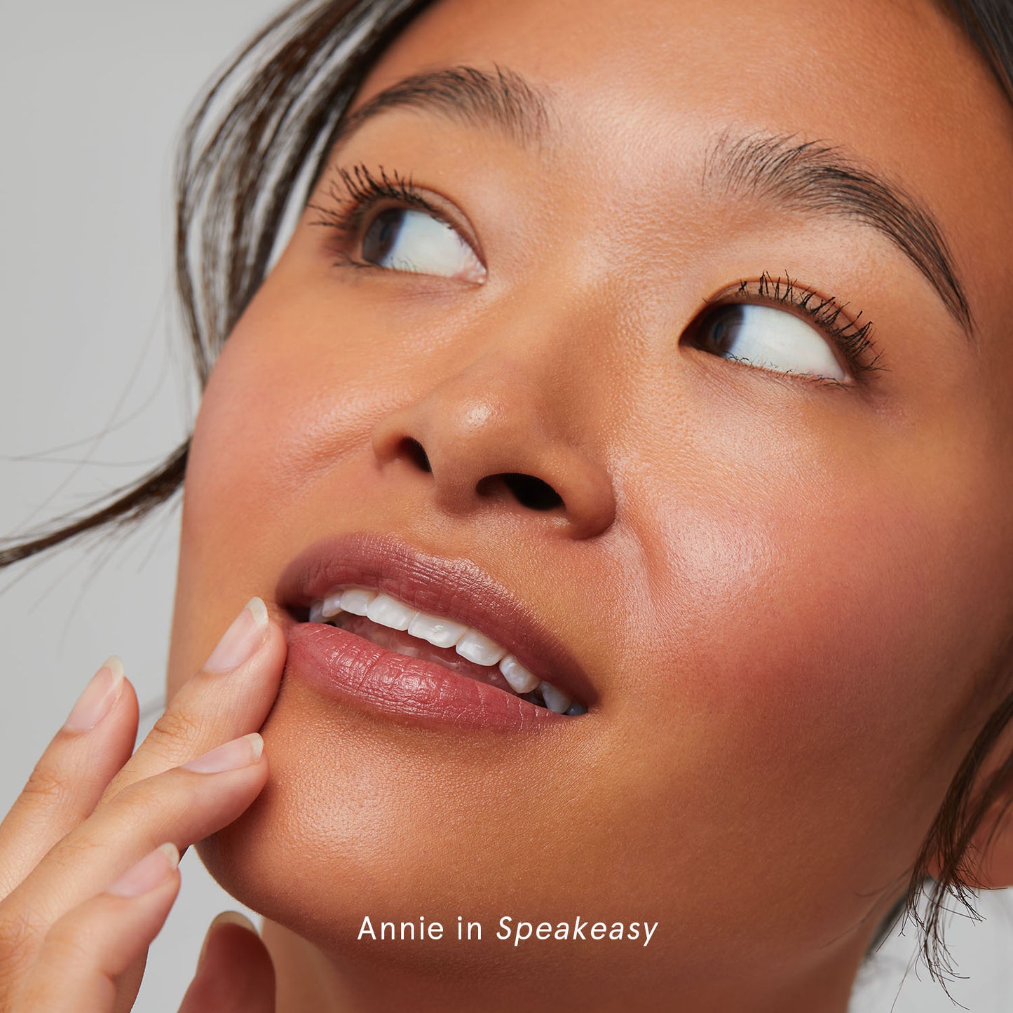 Close-up of a person looking upwards thoughtfully with hand near mouth.